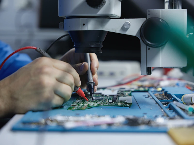 Technician inspecting electronic circuit board under microscope